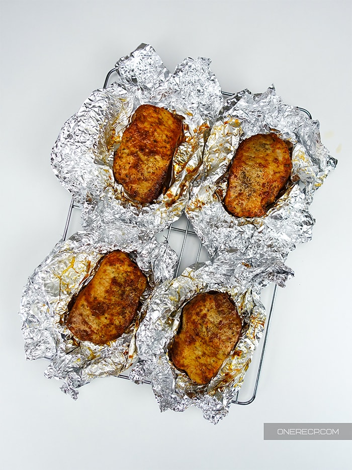 four frehsly baked pork chops resting in nests of aluminum foil