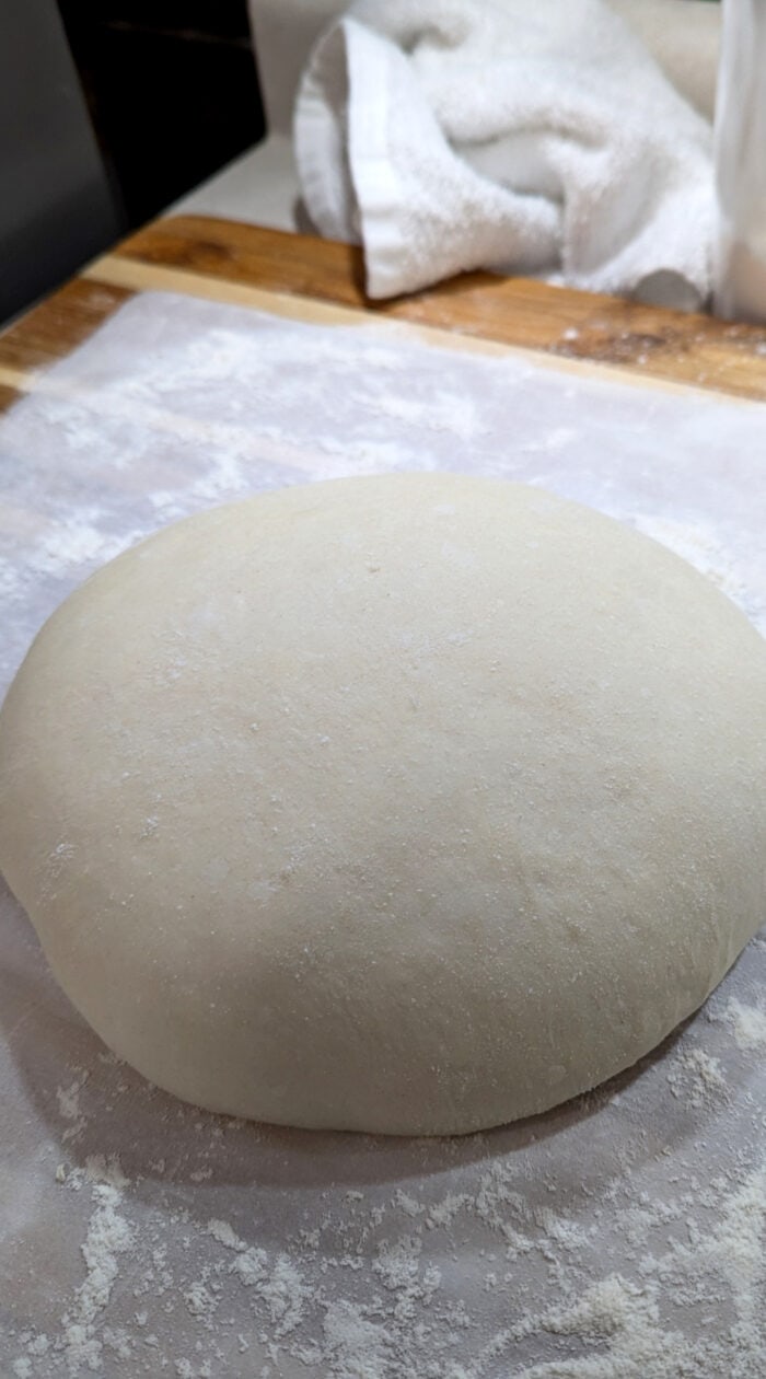 Ball of smooth, freshly kneaded dough resting on a floured surface ready for baking.