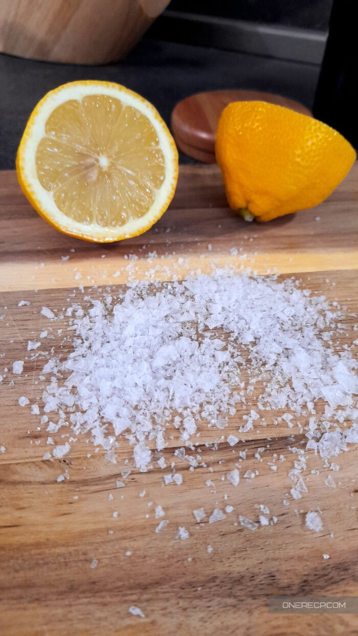 Coarse salt and a halved lemon on a wooden cutting board, ready for natural cleaning.