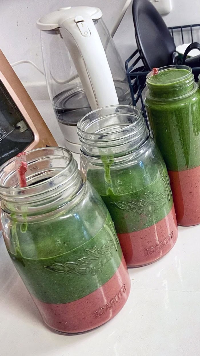 Three mason jars filled with layered green and berry smoothies prepared ahead of time for easy overnight storage in the fridge.