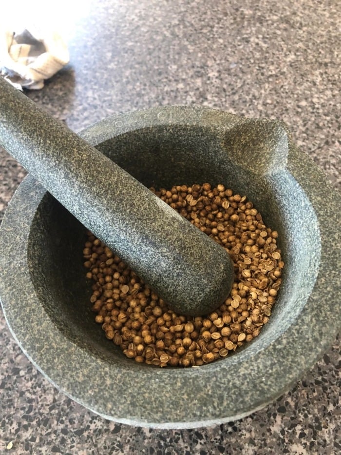 manually grinding coriander seeds by using a mortar and a pestle