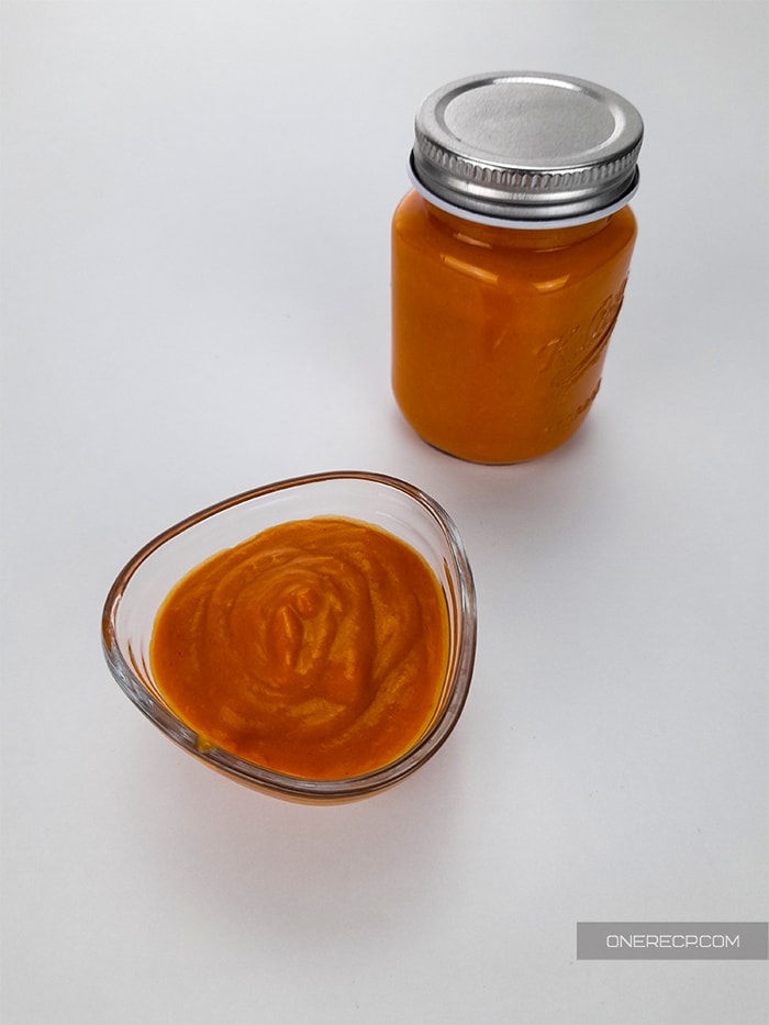 a glass cup of homemade buffalo wing sauce next to a small jar of the same