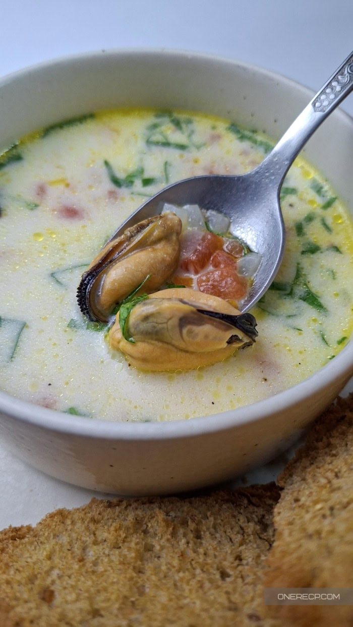 A spoonful of mussel soup with mussels, rice, and vegetables above a white bowl