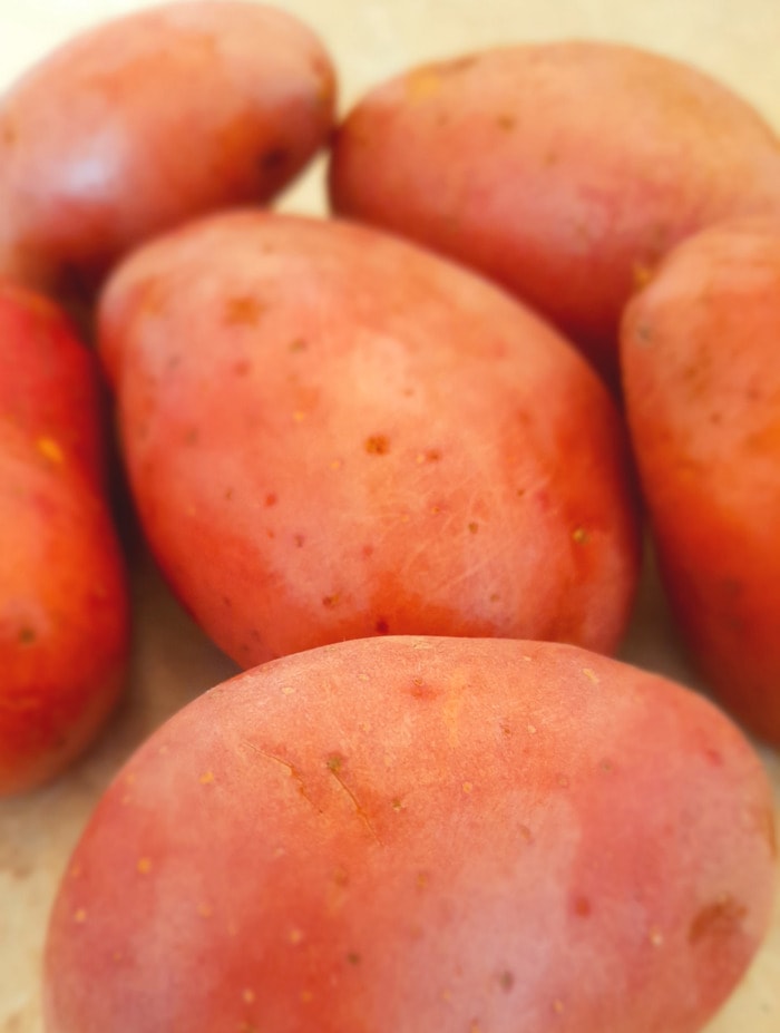 A close up of 6 slightly dusty red potatoes on a cutting board