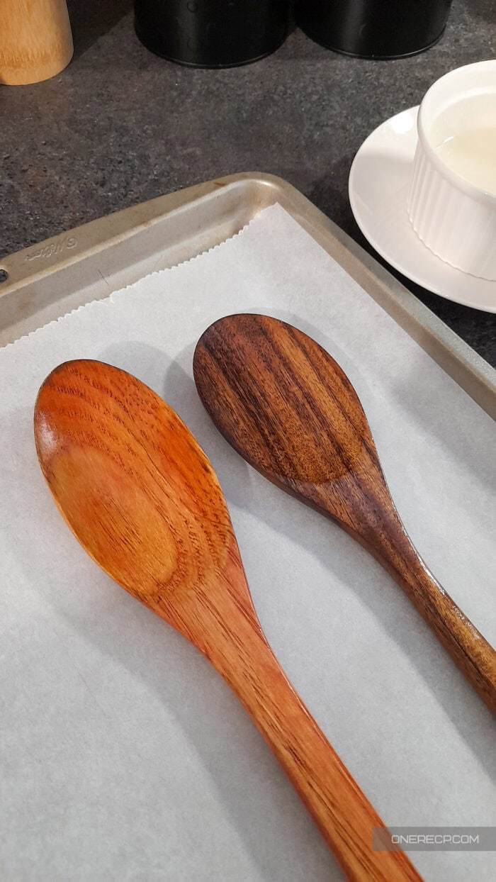Two wooden spoons coated with oil resting on parchment paper to allow full absorption before buffing.