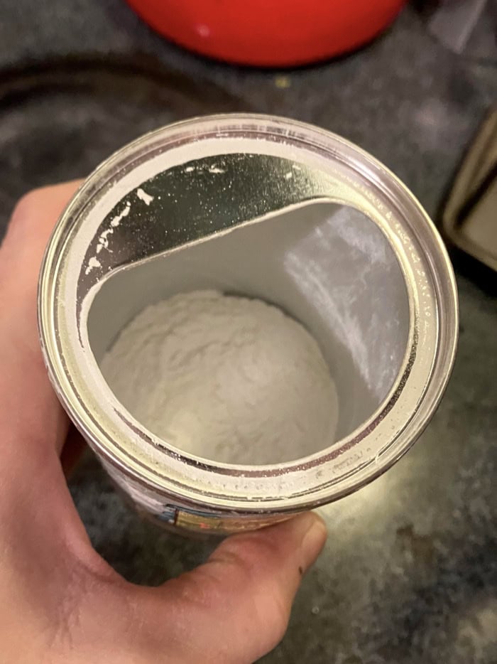 A hand holding an open container of baking powder, showing the powdery texture inside, ready for use in baking.