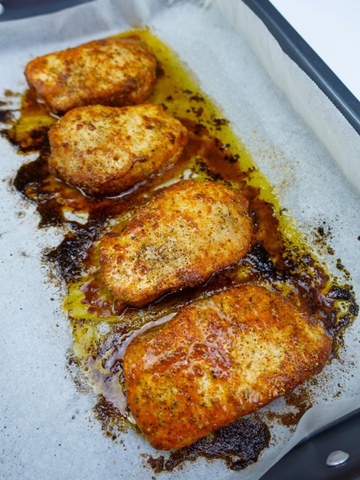 four freshly oven roasted pork chops in a baking tray