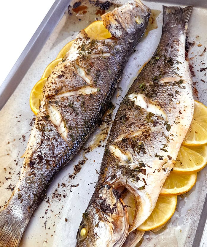 two oven roasted whole brazino fish stuffed with lemons in a baking tray