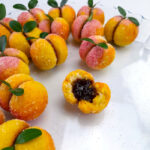 a batach of peach cookies with one showing the jam inside