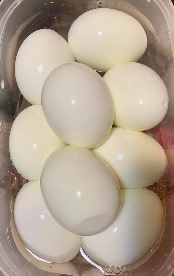 a couple of peeled hard boiled eggs in a plastic container with a little water ready to be stored in the refrigerator