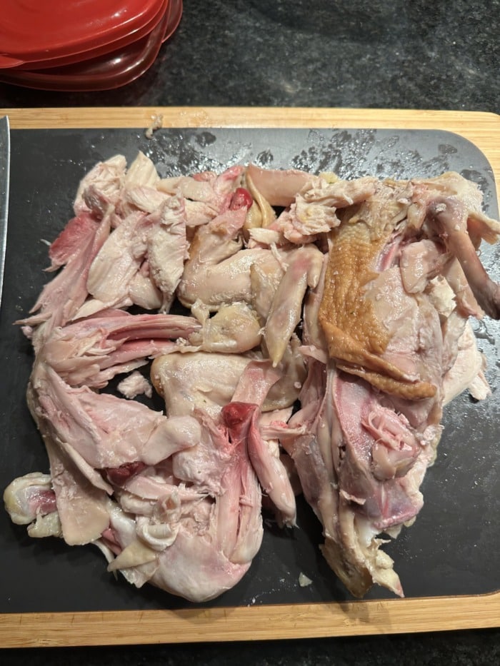 a wooden board of deconstructed pieces of cooked rotisserie chicken thighs with pink meat around the bones