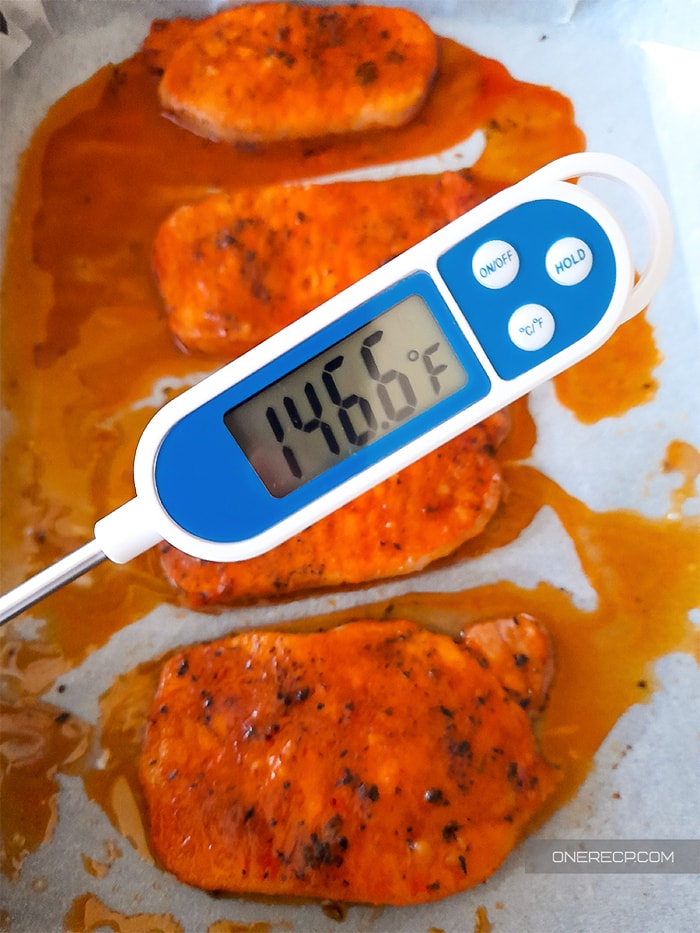 A cooking thermometer showing the internal temperature of the pork chops in the background