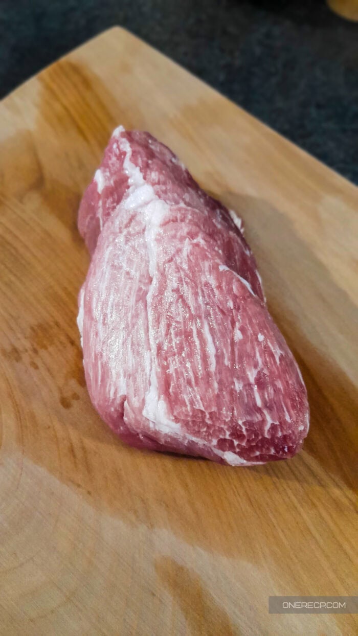 A piece of raw meat on a wooden cutting board before cleaning and disinfecting.