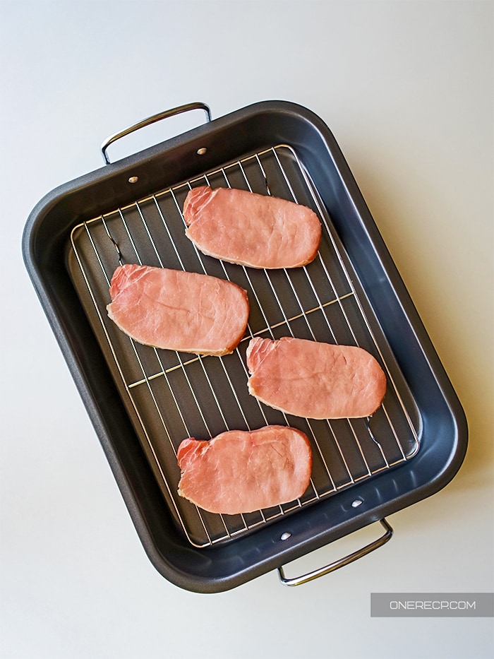 Raw pork chops on a baking tray with a wire rack