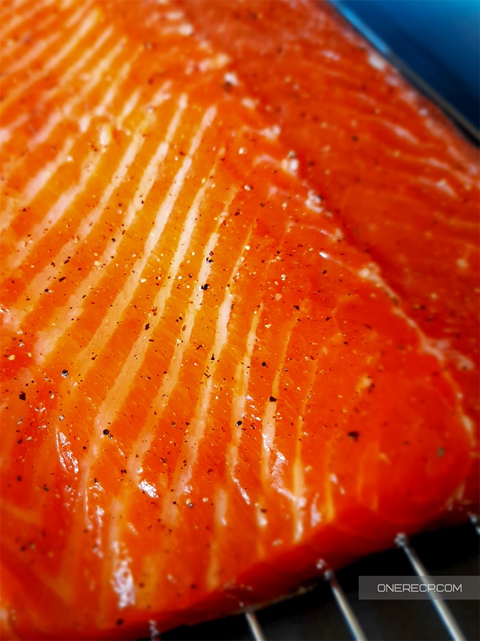 Close-up of a salmon fillet sprinkled with ingredients on a wire rack