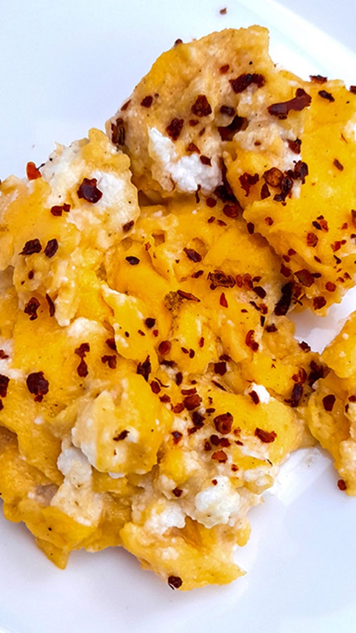 Creamy scrambled eggs with ricotta cheese topped with red pepper flakes, served on a white plate for a cozy Mediterranean-style breakfast.