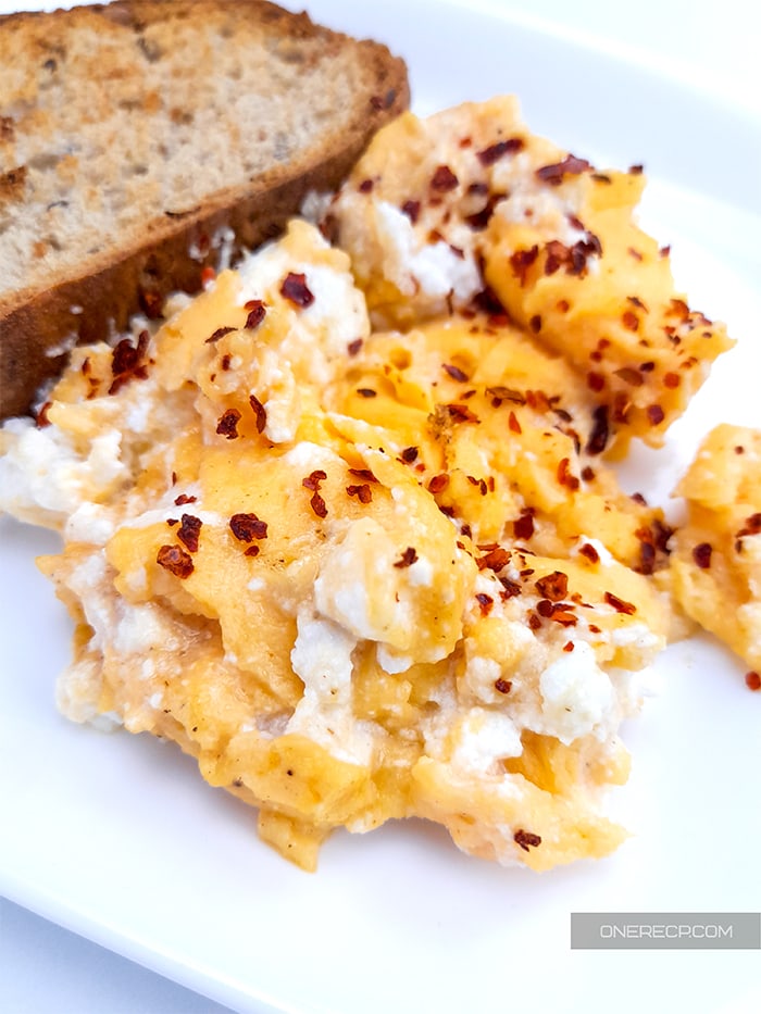 Close-up of scrambled eggs with ricotta cheese next to a slice of toasted bread