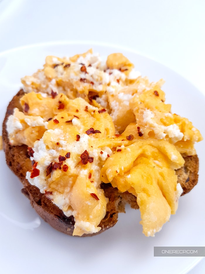 Scrambled eggs with ricotta cheese spread over a toast