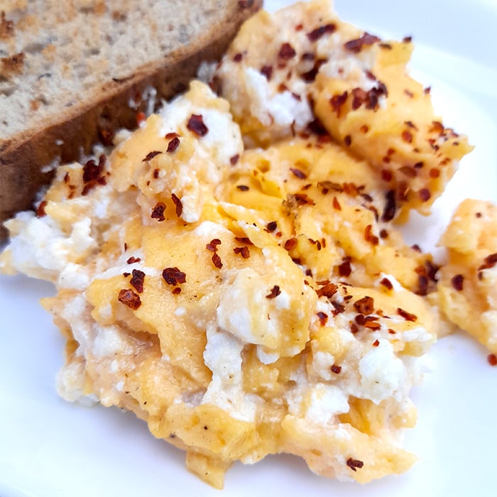 scrambled eggs with ricotta cheese next to a slice of toasted bread