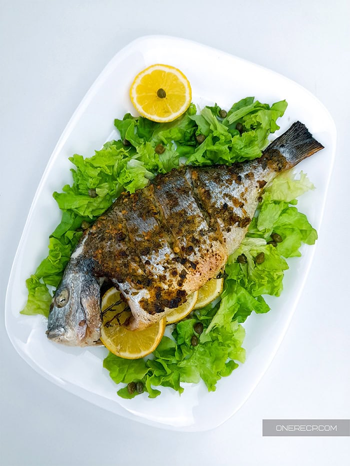 A serving of oven roasted sea bream garnished with lettuce and capers