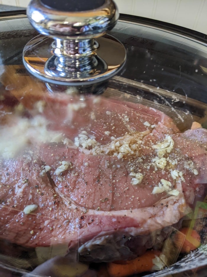 beef roast cooking under the lid of a slow cooker