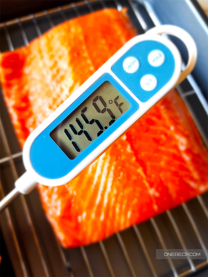 A cooking thermometer showing the internal temperature of the salmon fillet in the background