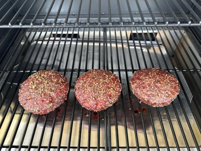 three seasoned burgers being smoked on a traeger grill 
