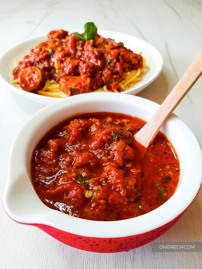 Spaghetti sauce without tomato paste in a small bowl with a wooden spoon and a plate of spaghetti in the background