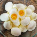 a bowl of peeled hard boiled eggs with the top one sliced in two