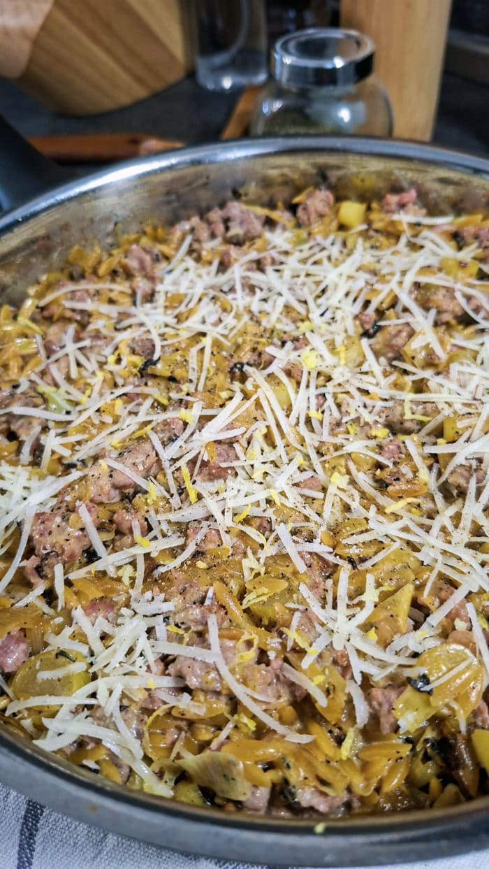 Creamy sweet Italian sausage orzo topped with freshly grated Parmesan, lemon zest, and cracked black pepper in a large skillet.
