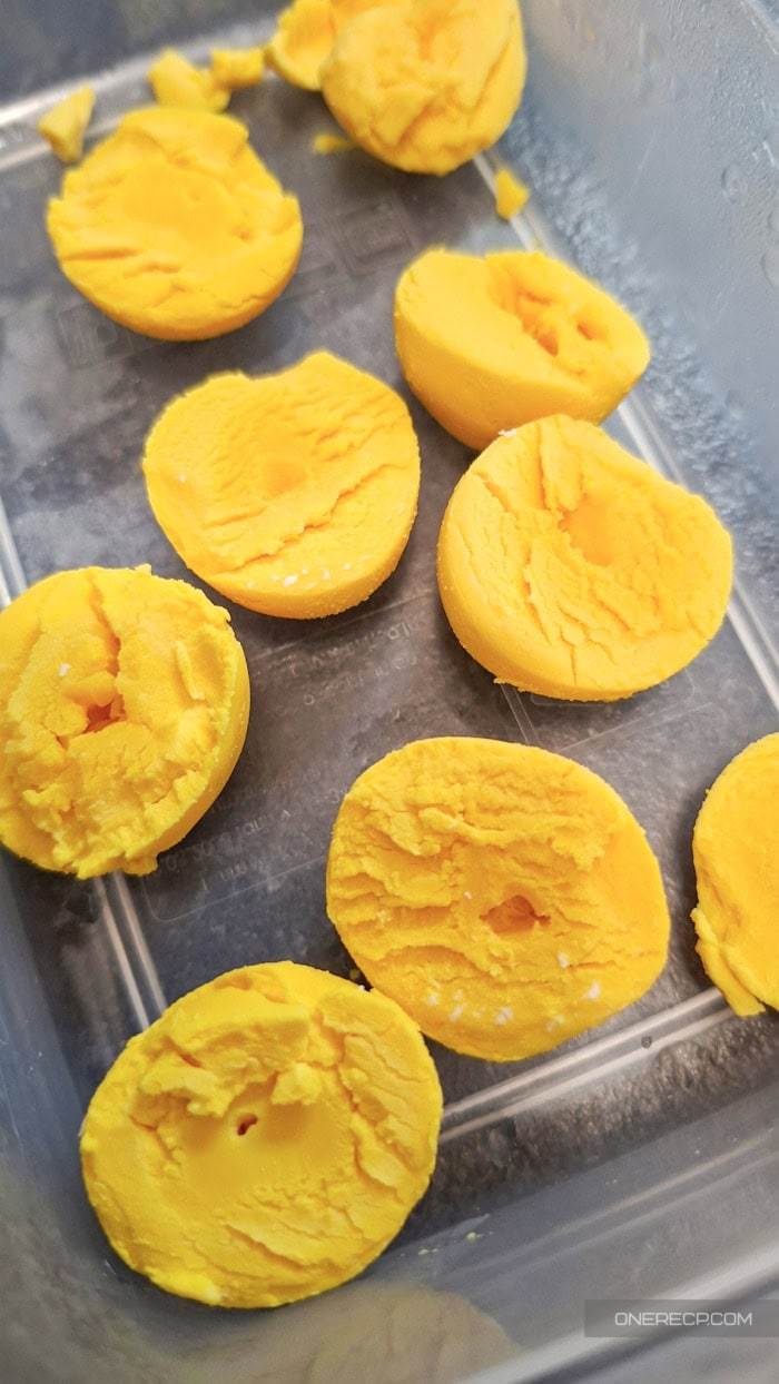 Thawed hard-boiled egg yolk halves in a freezer-safe container showing their texture after freezing.