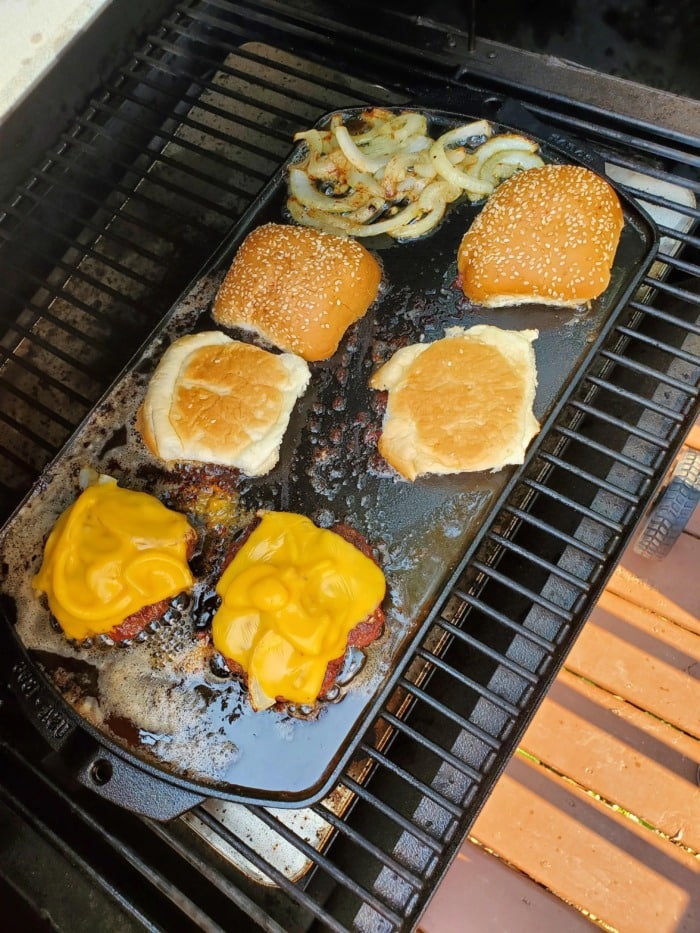 different components of burgers being grilled over a cast iron griddle on a treagere grill