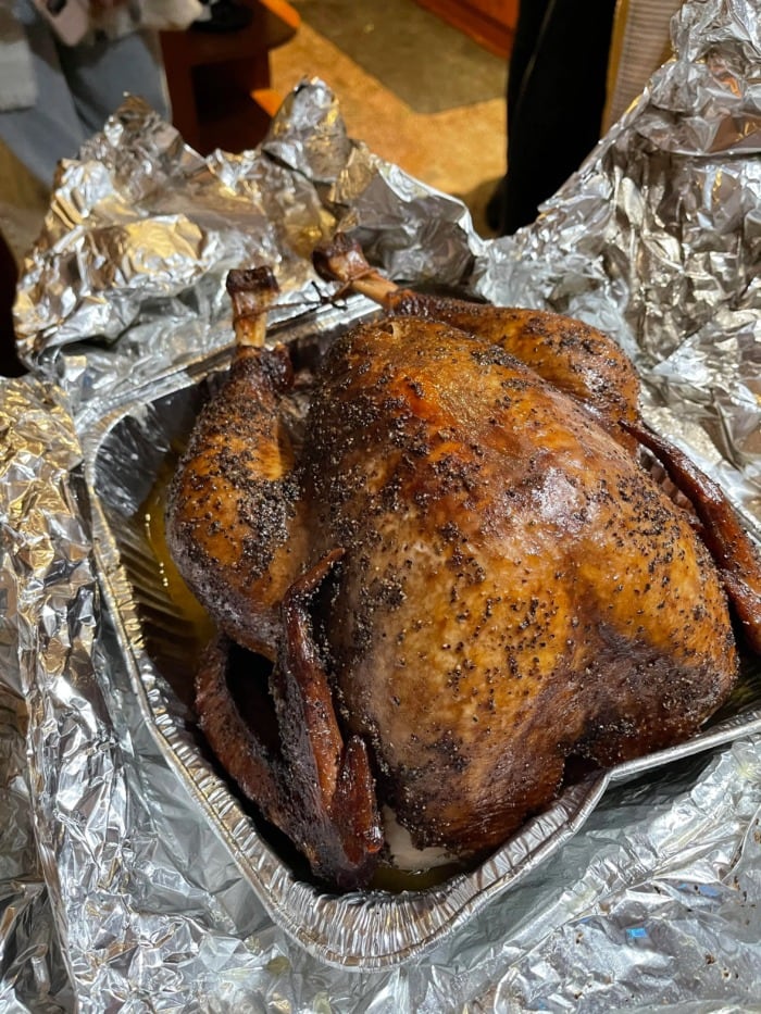 a whole cooked turkey in  an aluminum pan about to be wrapped in aluminum foil for resting