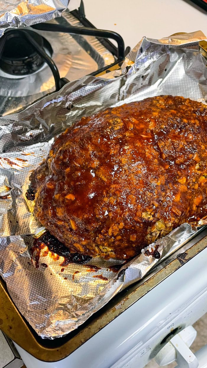 Homemade meatloaf baking uncovered on a foil-lined sheet pan with a dark caramelized crust forming on top.