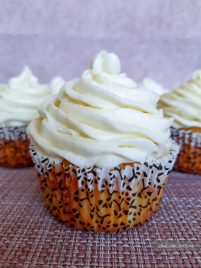 Close up of a baked vanilla cupcake with plenty of frosting on top