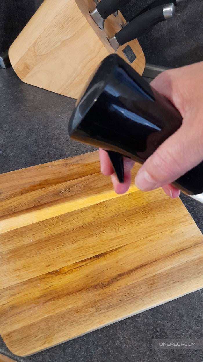 Hand spraying a wooden cutting board with a vinegar solution for natural disinfection.