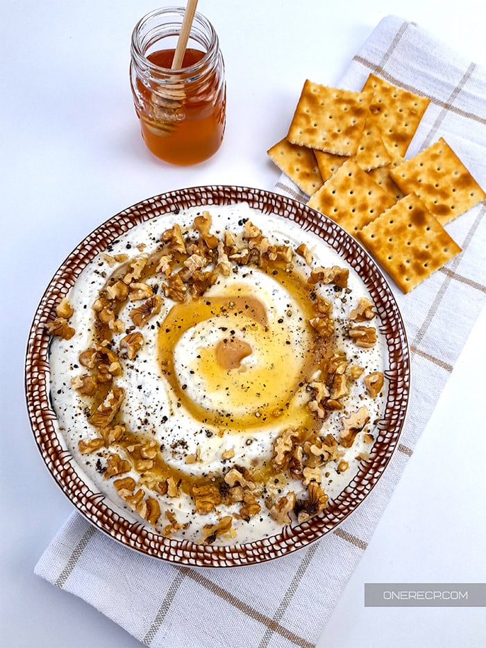 A bowl of whipped feta with honey next to some crackers and a jar of honey.