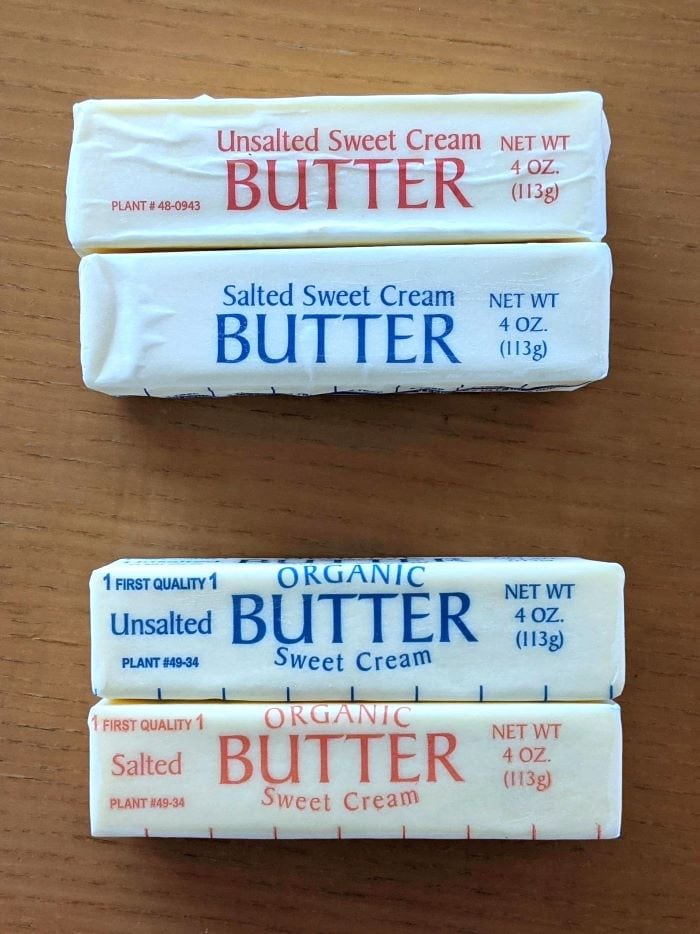 Four individually wrapped sticks of different types of butter with opposingly colored text on each of the labels between the organic and non-organic options of salted and unsalted butter