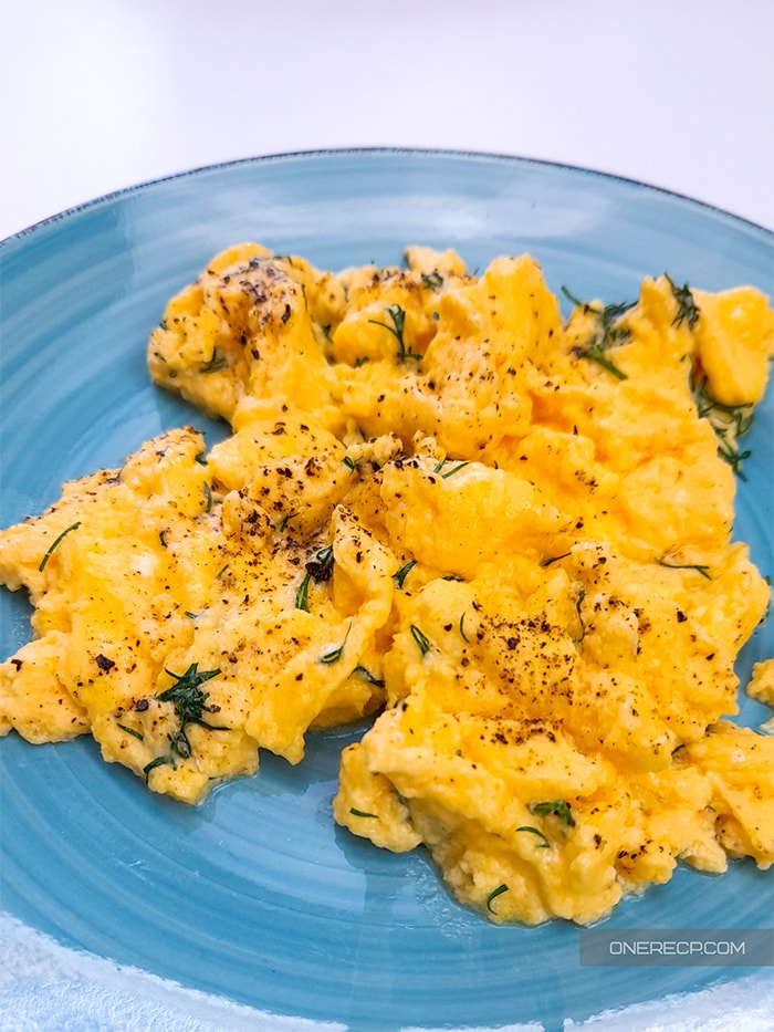 A plate with scrambled eggs seasoned with ground pepper and dill